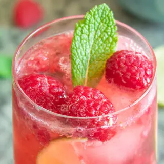 Raspberry caipiroska surrounded by raspberries and lime