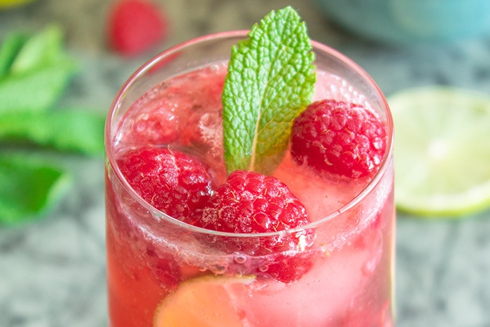 Raspberry caipiroska surrounded by raspberries and lime