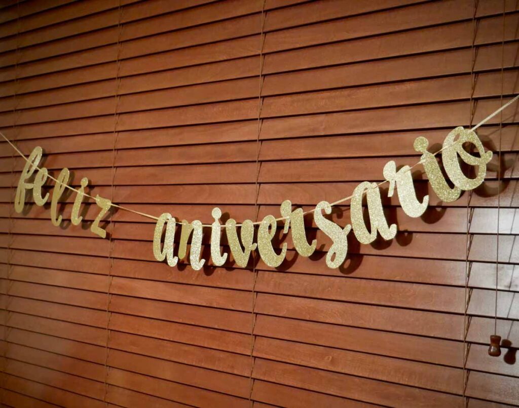 Gold and glitter lettering sign that reads "Feliz Aniversario" on a window, which means happy birthday in Brazilian Portuguese